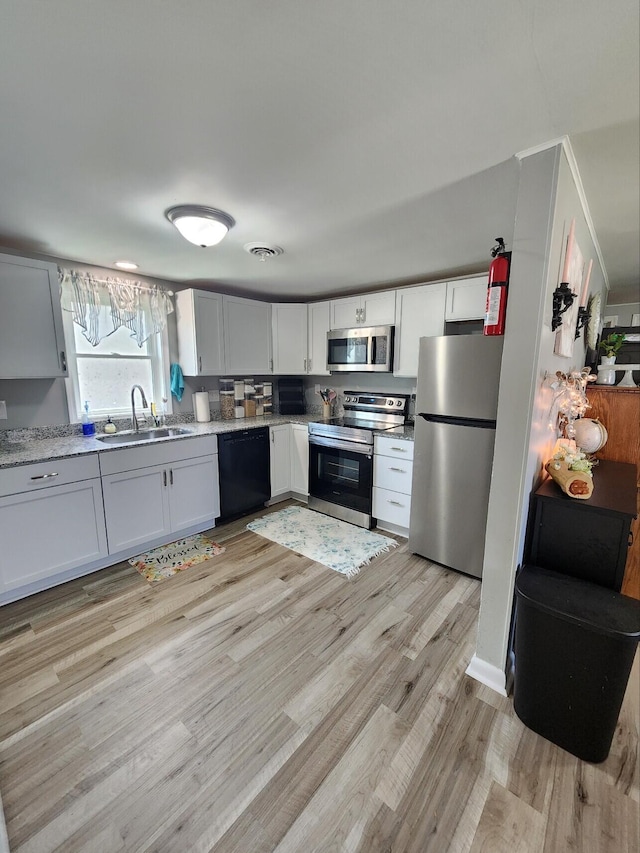 kitchen with appliances with stainless steel finishes, a sink, and light wood finished floors