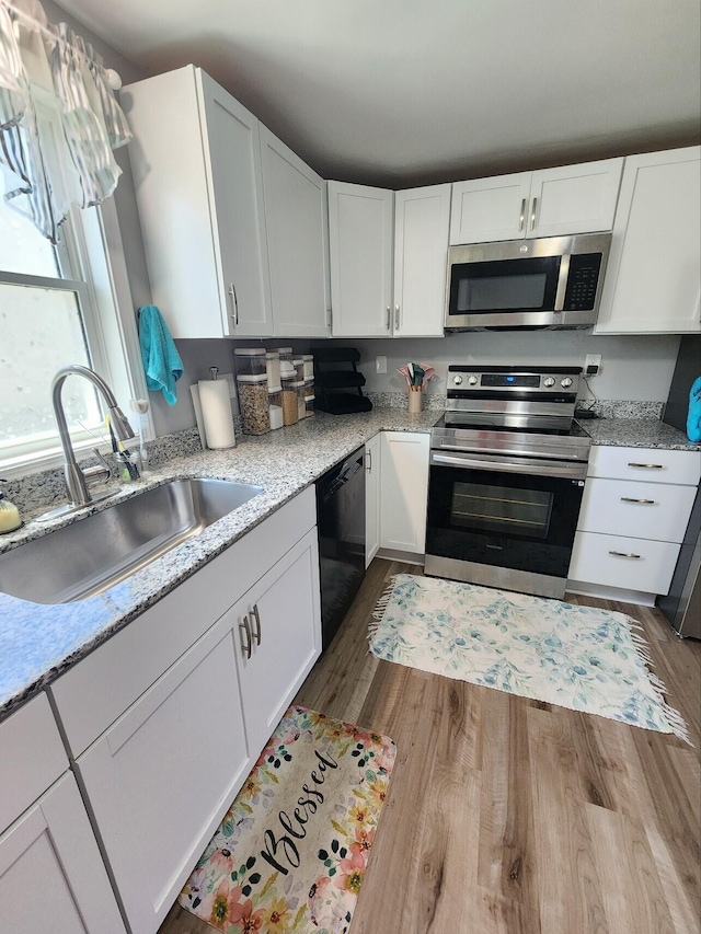 kitchen with appliances with stainless steel finishes, a sink, dark wood finished floors, and white cabinetry