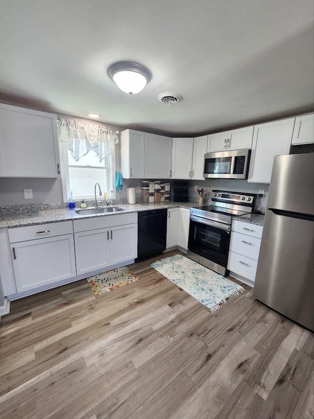 kitchen with appliances with stainless steel finishes, white cabinetry, a sink, light wood-style flooring, and light stone countertops