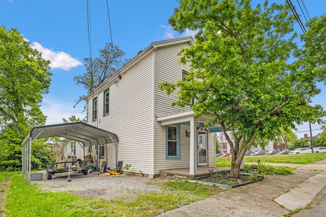view of side of home with gravel driveway, a carport, and covered porch
