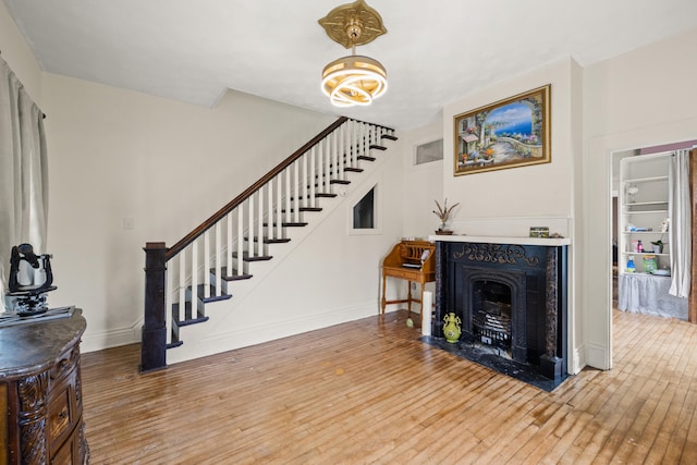 living room with stairs, light wood-style floors, baseboards, and a fireplace with flush hearth