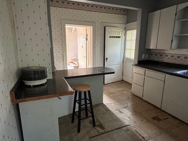kitchen featuring open shelves, dark countertops, wallpapered walls, white cabinetry, and a kitchen breakfast bar