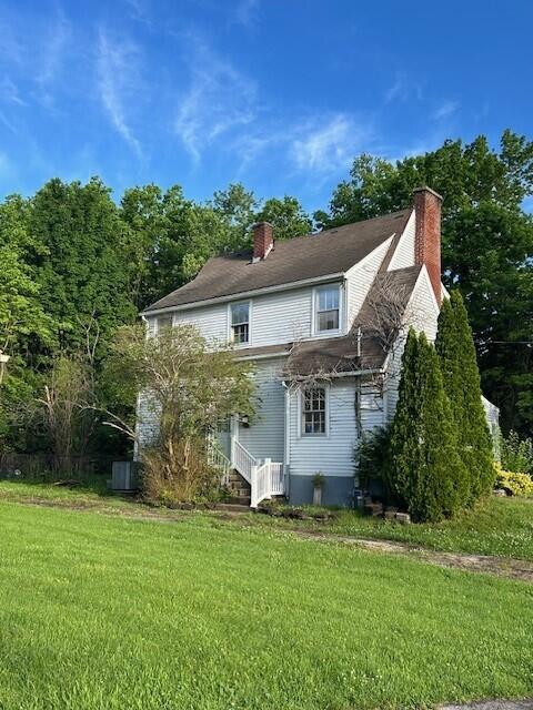 rear view of house featuring a chimney and a lawn