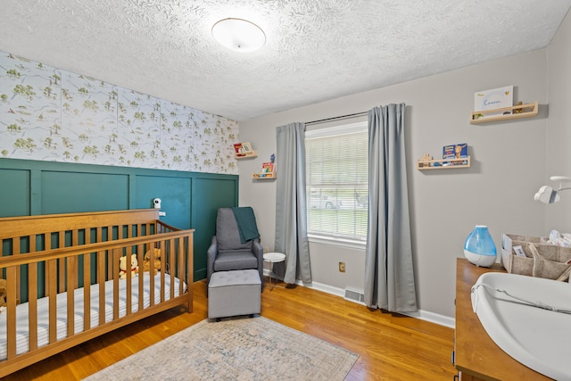 3540 Cornwall Dr, Lexington, KY 40503 - bedroom with wallpapered walls, wood finished floors, a crib, a wainscoted wall, and a textured ceiling