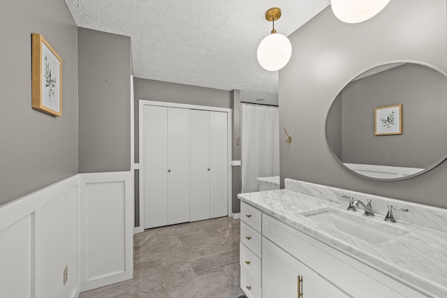 3540 Cornwall Dr, Lexington, KY 40503 - bathroom with vanity, marble look tiles, a textured ceiling, and a wainscoted wall