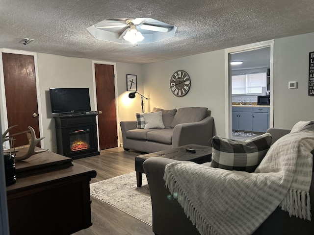842 Lower Cane Creek Rd, Stanton, KY 40380 - living room featuring dark wood-type flooring, a textured ceiling, ceiling fan, and a glass covered fireplace