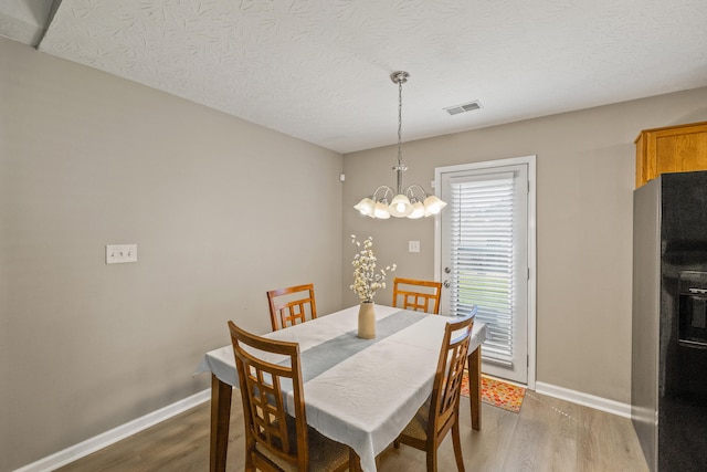 dining area featuring a chandelier, wood finished floors, baseboards, and a textured ceiling