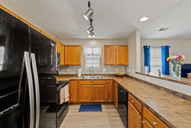 kitchen with black appliances, a sink, healthy amount of natural light, brown cabinetry, and a textured ceiling