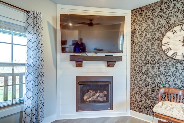 living area featuring wallpapered walls, baseboards, a ceiling fan, wood finished floors, and a glass covered fireplace