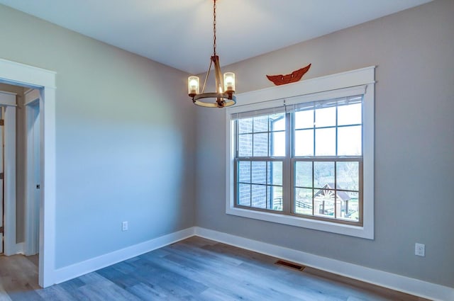 spare room featuring a chandelier, baseboards, and wood finished floors