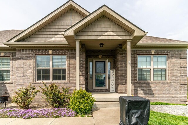 view of exterior entry featuring brick siding and roof with shingles