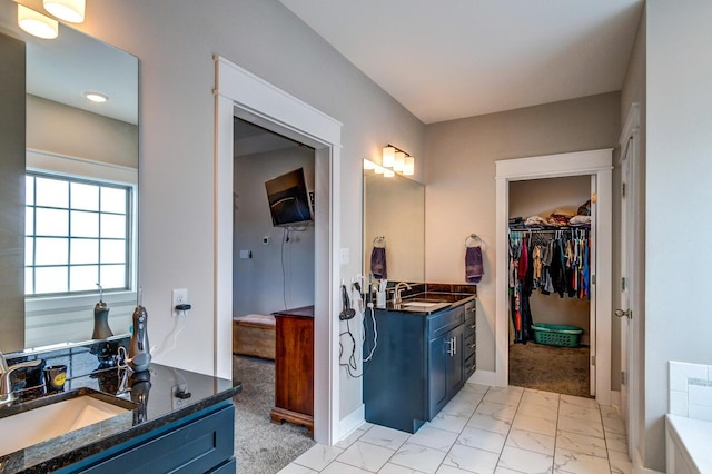 bathroom with two vanities, a walk in closet, marble finish flooring, and baseboards