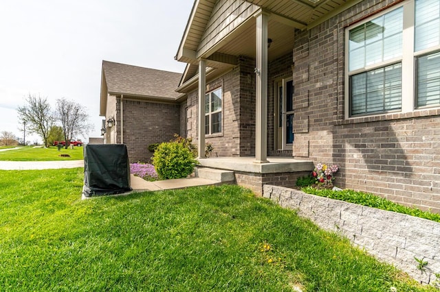 view of exterior entry featuring a lawn, brick siding, and covered porch