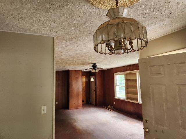 unfurnished room featuring a chandelier, a textured ceiling, wooden walls, and a ceiling fan