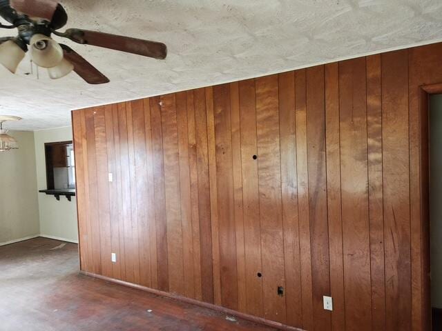 unfurnished room with a ceiling fan, wood walls, and baseboards