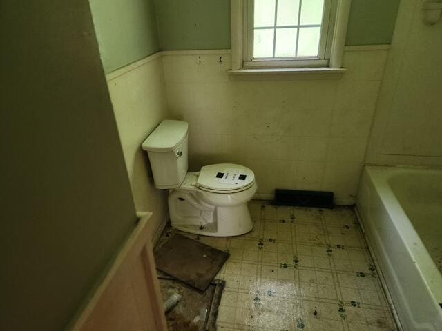 bathroom featuring toilet, a wainscoted wall, a bathtub, tile patterned floors, and tile walls