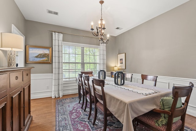dining area featuring a chandelier, wood finished floors, a wainscoted wall, and a decorative wall