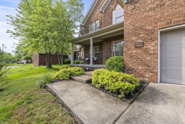 property entrance with covered porch, brick siding, a yard, and a garage