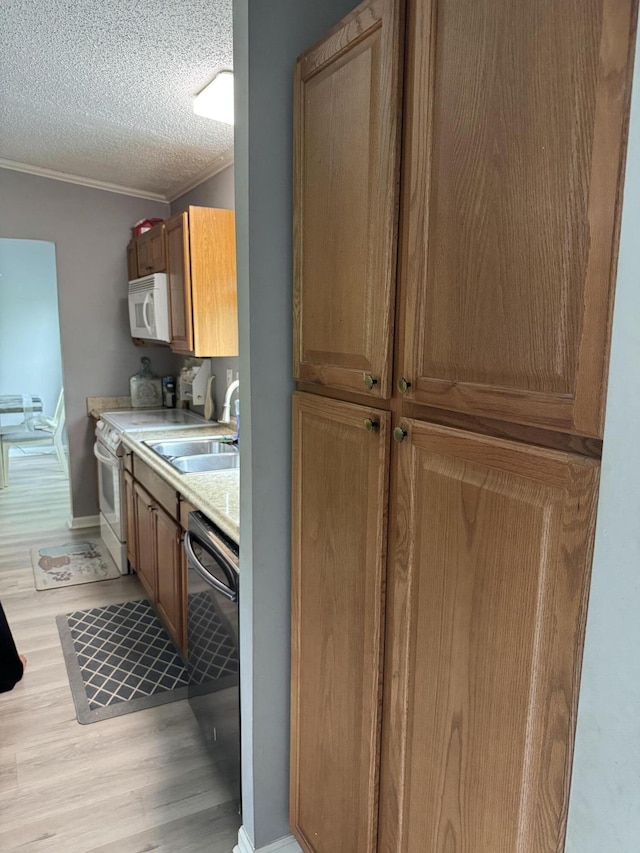 kitchen featuring white appliances, light wood-style floors, light countertops, a sink, and crown molding
