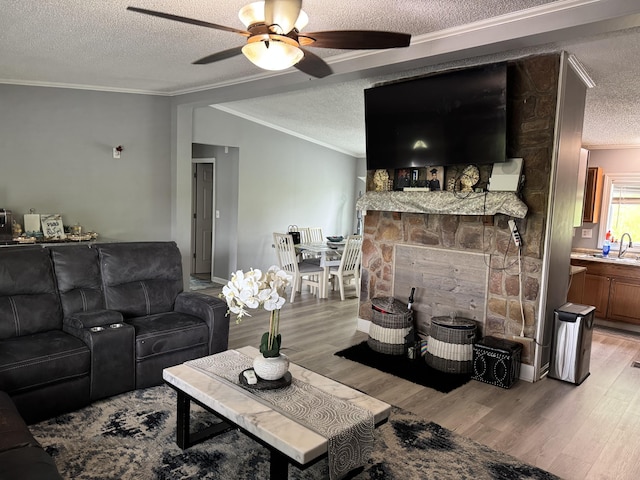 living area featuring a textured ceiling, ceiling fan, light wood finished floors, crown molding, and vaulted ceiling