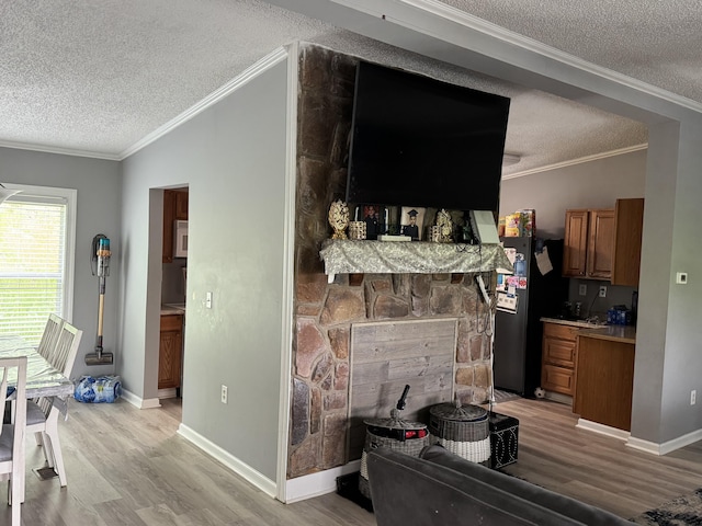living area featuring a textured ceiling, light wood-type flooring, baseboards, ornamental molding, and a stone fireplace