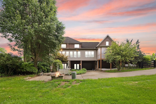 187 Woodside Dr, Somerset, KY 42503 - back of property at dusk featuring a fire pit, driveway, a garage, a lawn, and a patio