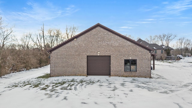 view of snow covered exterior featuring a garage and brick siding