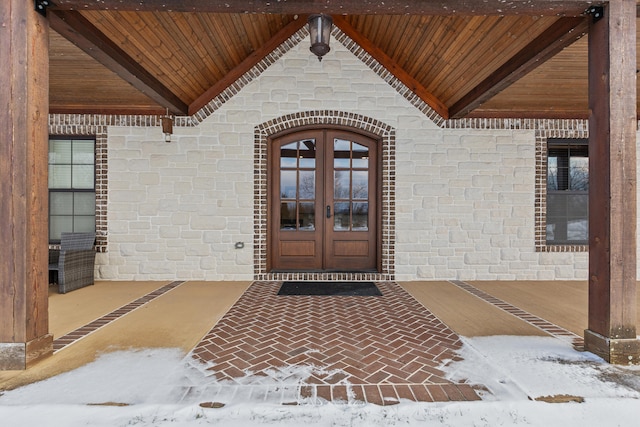 snow covered property entrance with french doors and stone siding