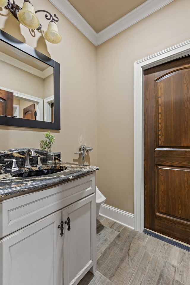 half bath with ornamental molding, wood finished floors, vanity, baseboards, and toilet