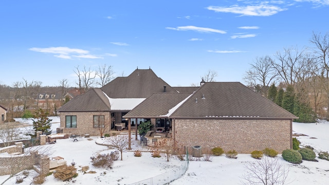 snow covered house with a patio area and brick siding