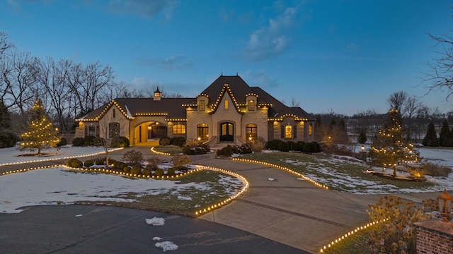 view of front of property with stone siding, curved driveway, and a chimney