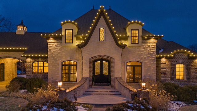 french provincial home with stone siding, french doors, entry steps, and brick siding