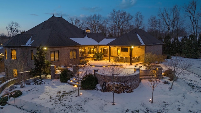 snow covered rear of property featuring brick siding, a patio, and a chimney