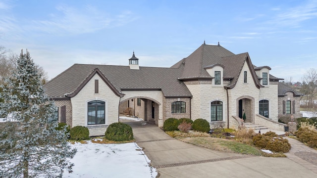 french country style house with stone siding, roof with shingles, and brick siding