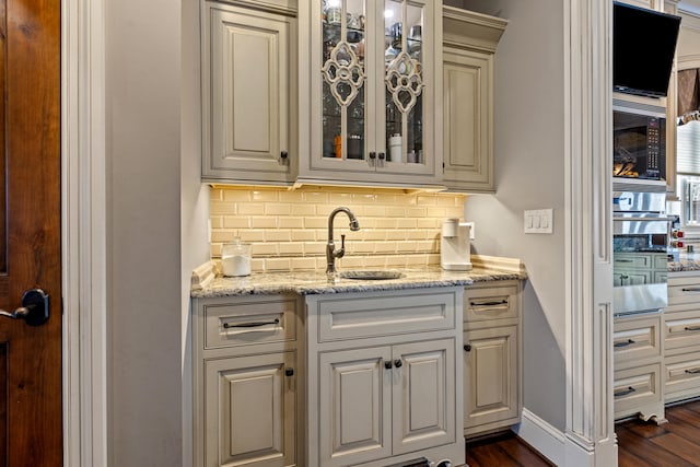 bar featuring a sink, tasteful backsplash, dark wood-style flooring, and baseboards