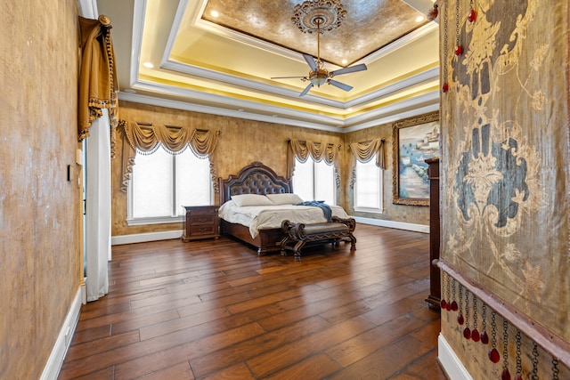 bedroom with a tray ceiling, baseboards, crown molding, multiple windows, and wood-type flooring