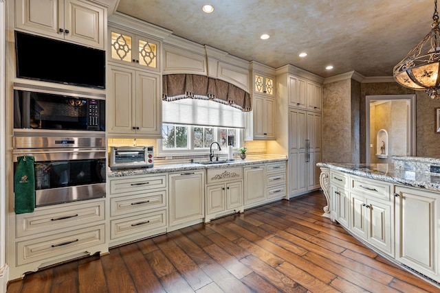 kitchen featuring stainless steel oven, cream cabinets, a sink, dark wood-style floors, and crown molding