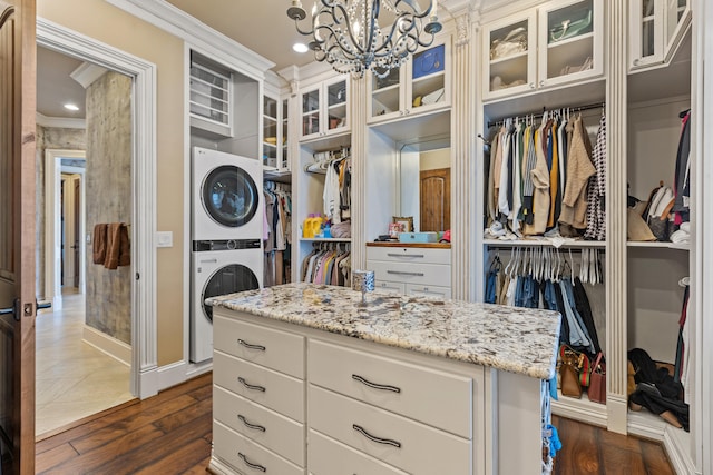 walk in closet with stacked washer / drying machine, dark wood-type flooring, and a chandelier