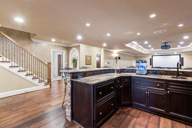 kitchen featuring a sink, ornamental molding, a kitchen bar, dark wood-style flooring, and dark stone counters