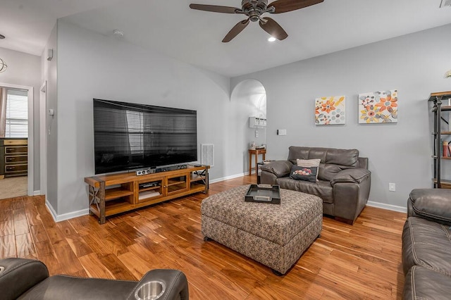 living area with arched walkways, a ceiling fan, wood finished floors, and baseboards