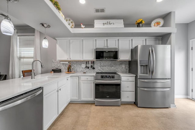 kitchen with appliances with stainless steel finishes, a sink, decorative backsplash, light countertops, and white cabinetry