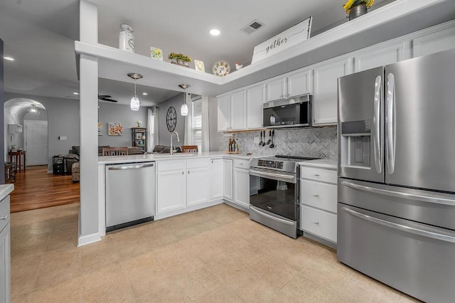 kitchen featuring appliances with stainless steel finishes, a sink, light countertops, arched walkways, and white cabinets