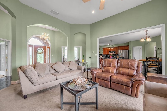 living room featuring arched walkways, light colored carpet, a chandelier, a ceiling fan, and a high ceiling