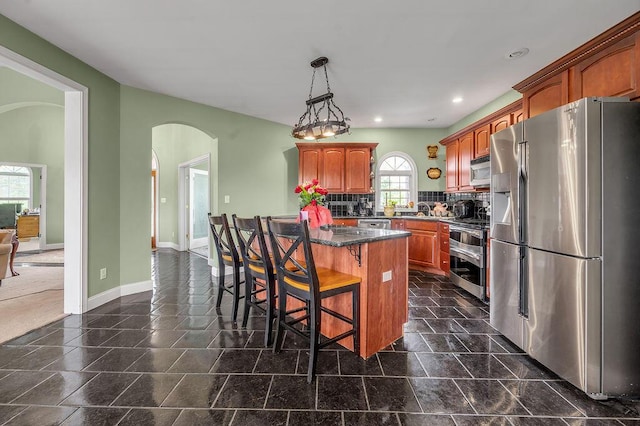 kitchen with appliances with stainless steel finishes, arched walkways, a breakfast bar area, recessed lighting, and baseboards