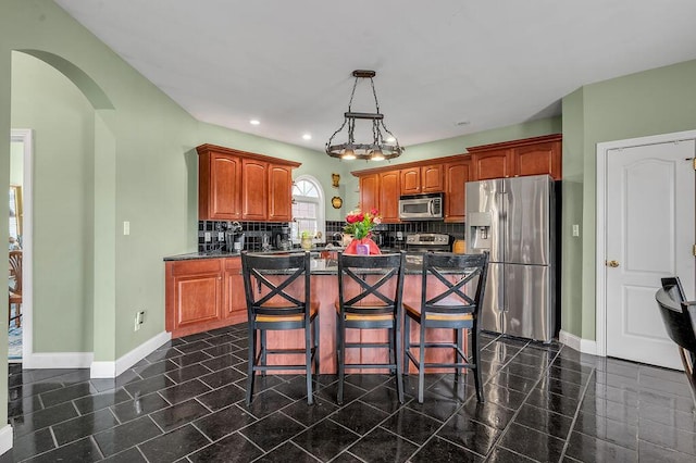 kitchen featuring stainless steel appliances, arched walkways, baseboards, a center island, and decorative backsplash
