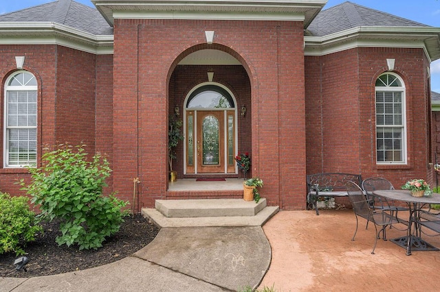 doorway to property featuring brick siding, a shingled roof, outdoor dining space, and a patio