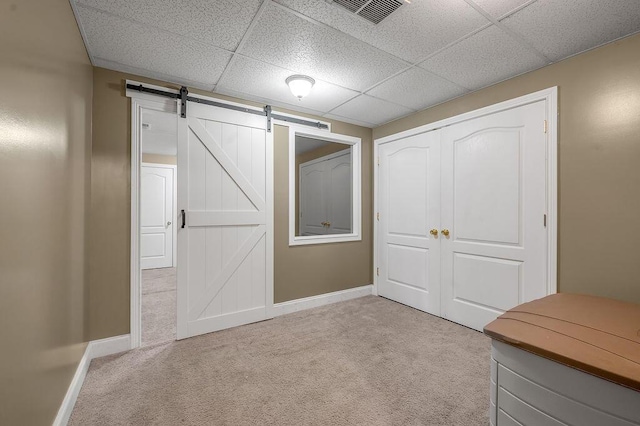 unfurnished bedroom featuring light colored carpet, baseboards, a barn door, a closet, and a paneled ceiling