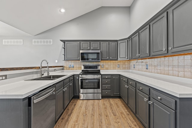 kitchen featuring stainless steel appliances, a sink, lofted ceiling, gray cabinetry, and light wood finished floors