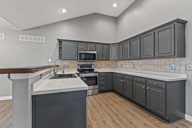 kitchen featuring appliances with stainless steel finishes, a sink, gray cabinets, light wood-style floors, and high vaulted ceiling