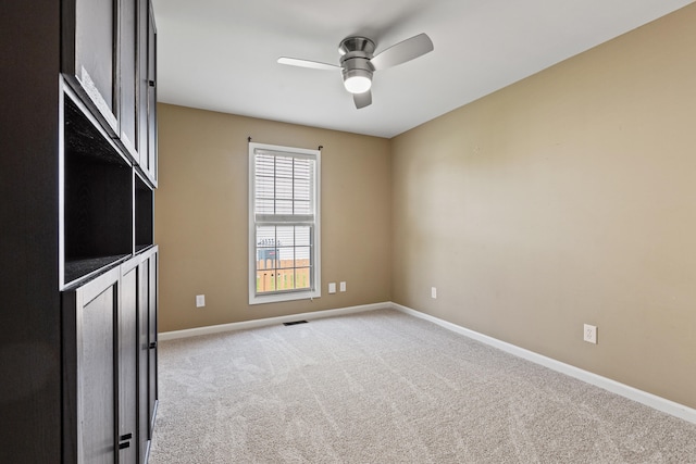 spare room with a ceiling fan, light colored carpet, and baseboards